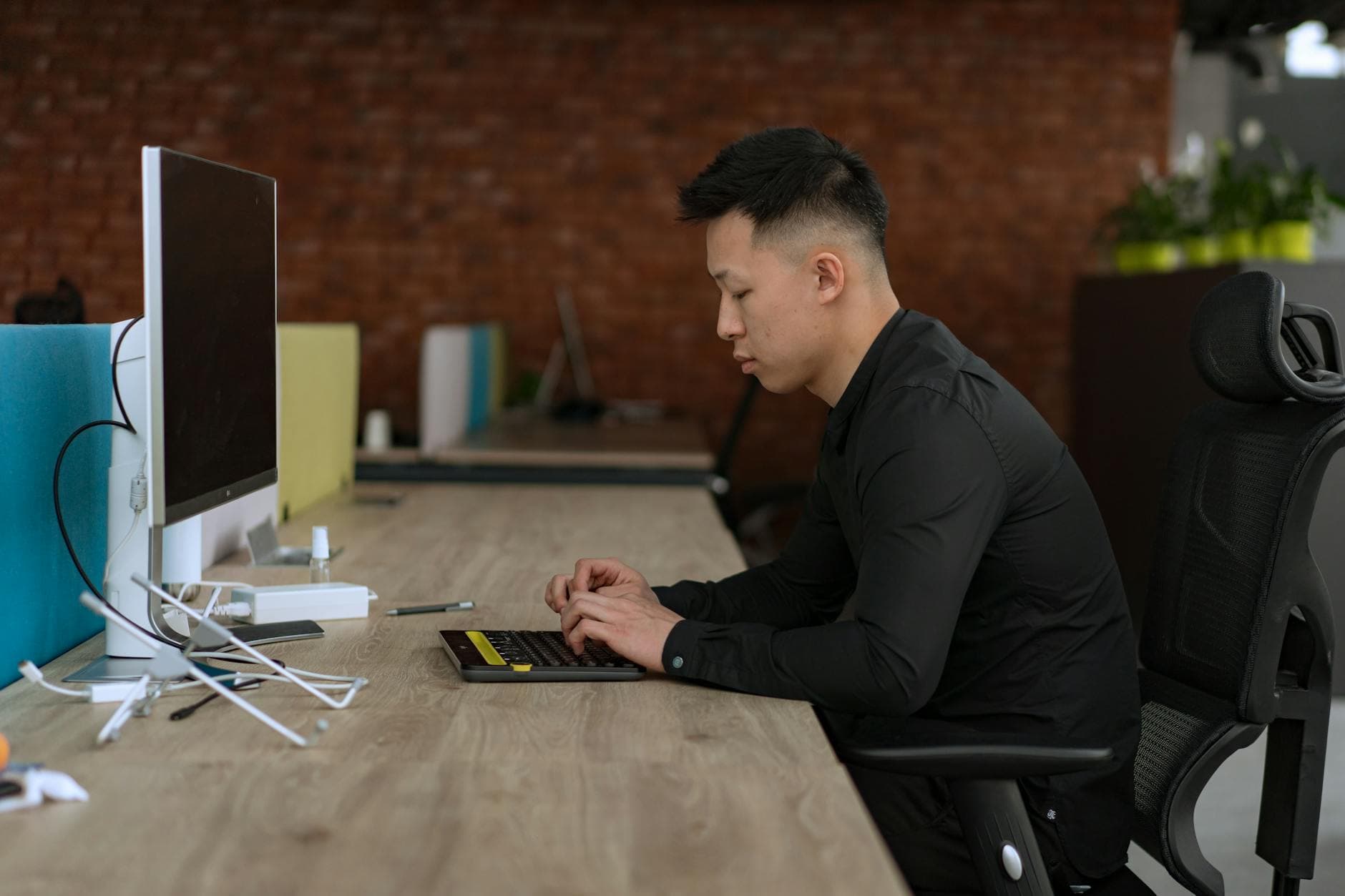 Asian man working on a computer in a modern office setting, focusing on productivity.