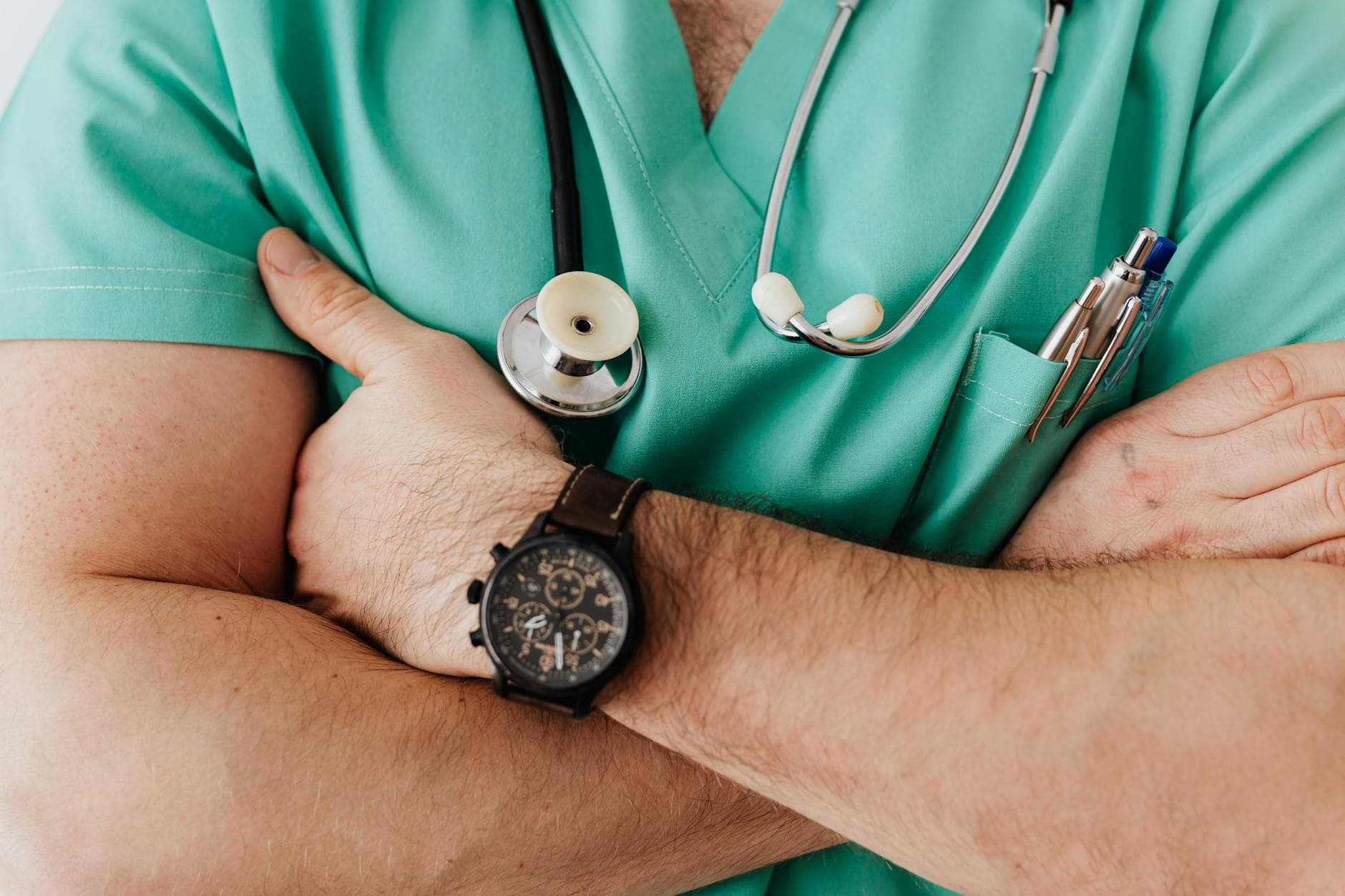 Unrecognizable female doctor in medical uniform with wristwatch on hand crossing arms on chest while standing with stethoscope on neck